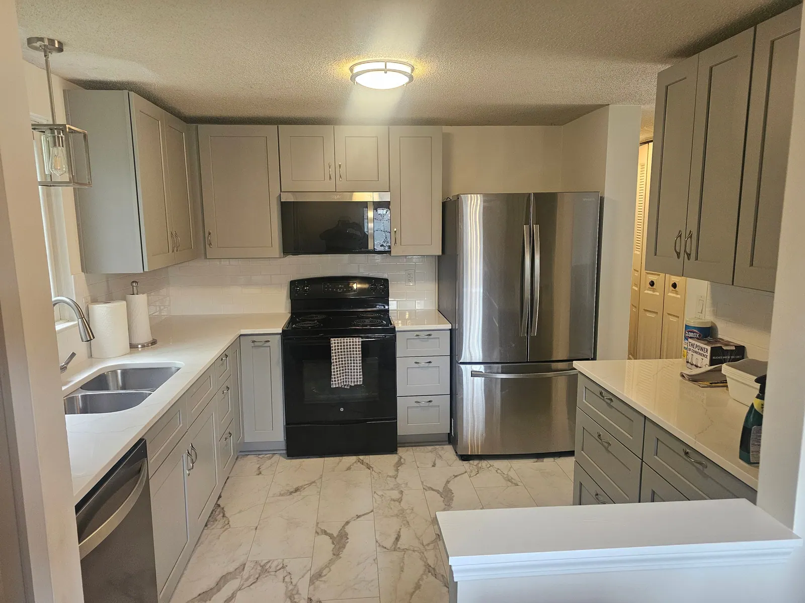 Remodeled kitchen with gray shaker cabinets, light counters and stainless appliances