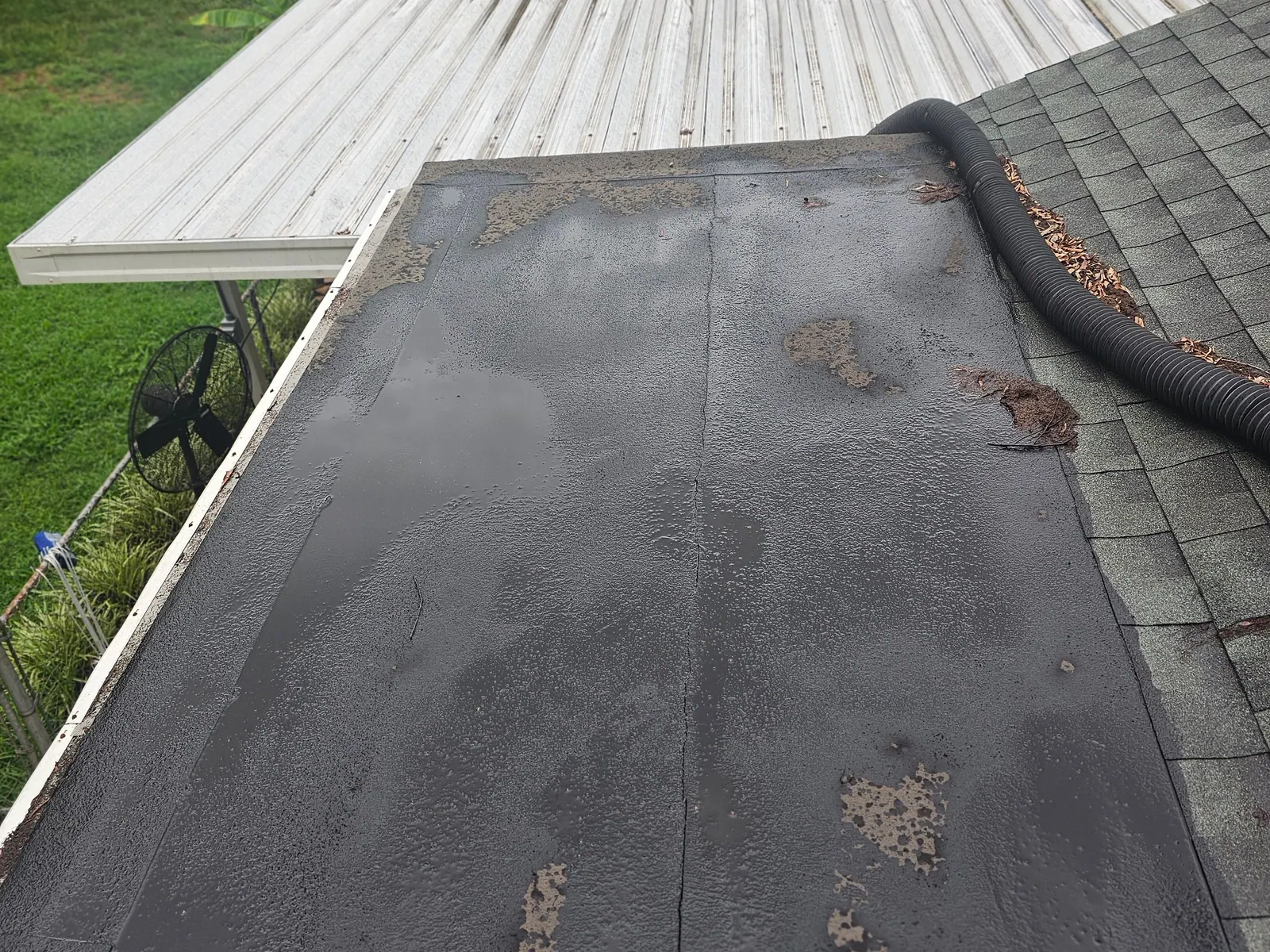 Worn low-slope roof section beside a patio cover before repair