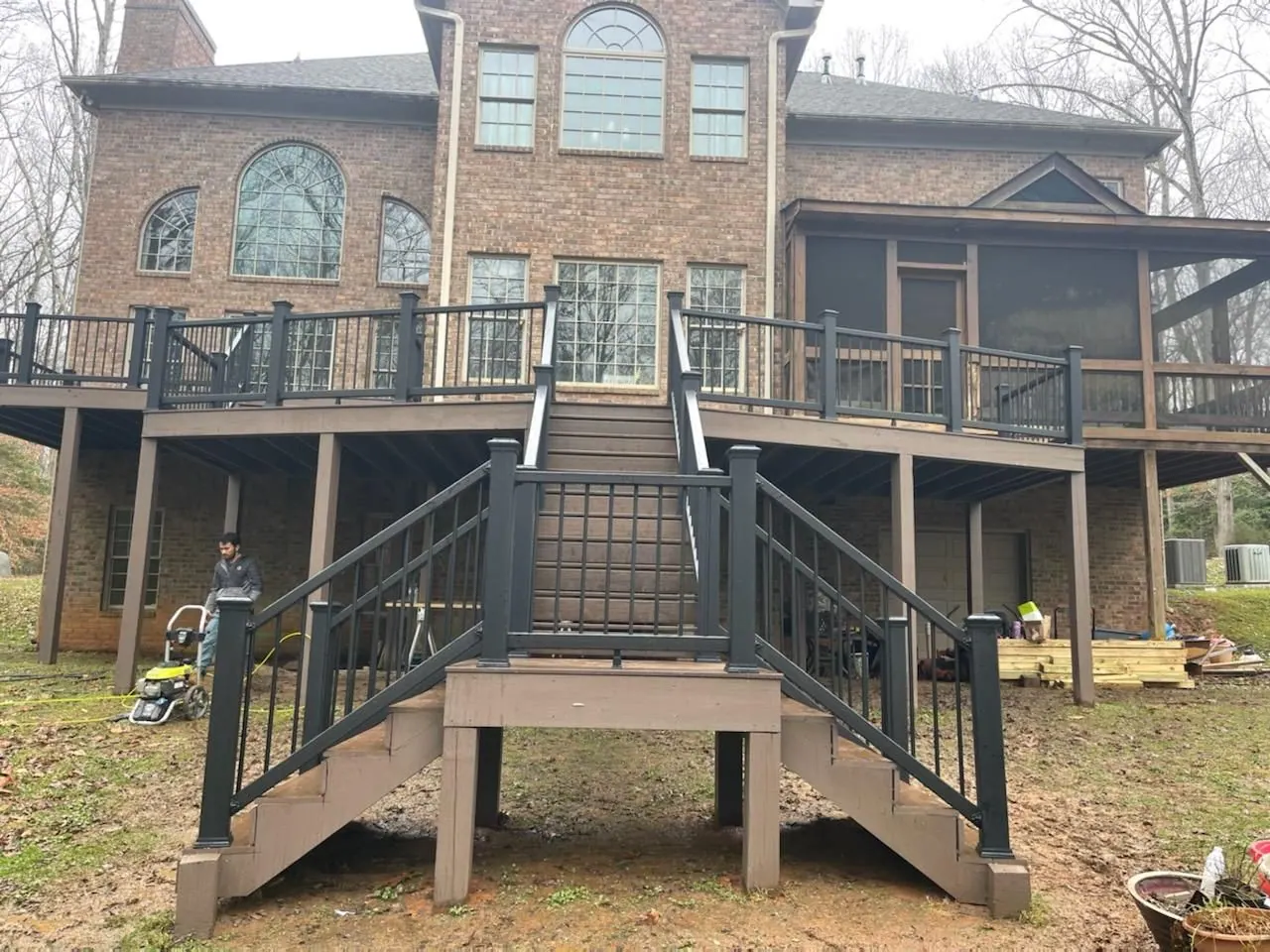 Multi-tier deck with stairs and dark railing behind a brick home