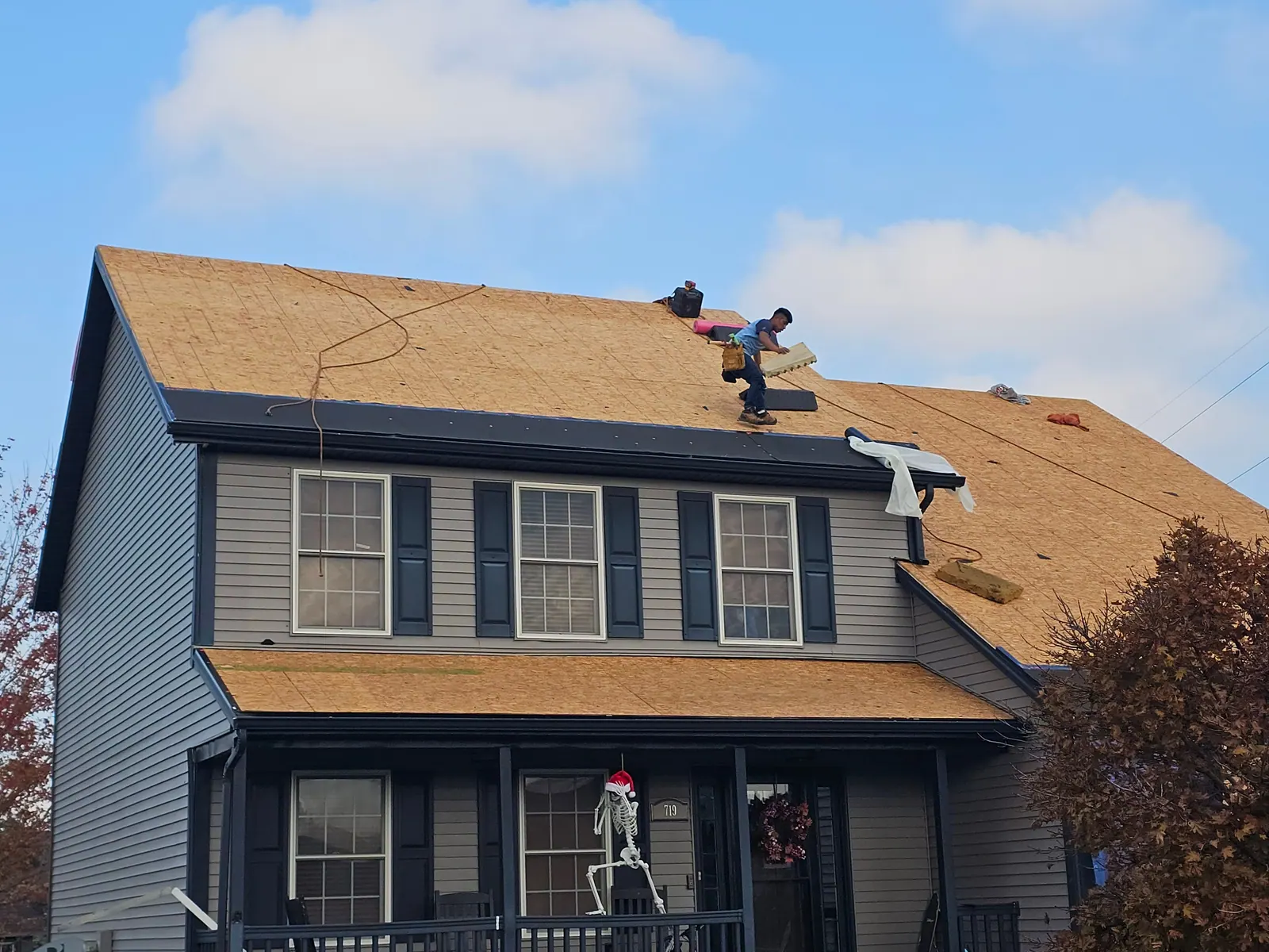 Roofers working on bare roof decking on a two-story home